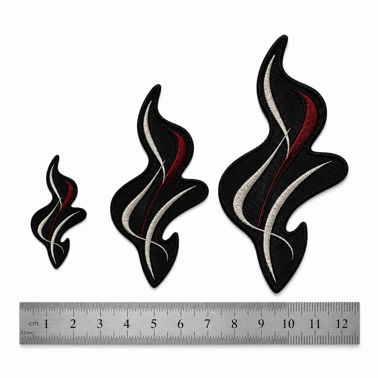 Trois tailles du même écusson brodé alignées au-dessus d'un réglet gradué en centimètres, de 4 à 12 cm de hauteur