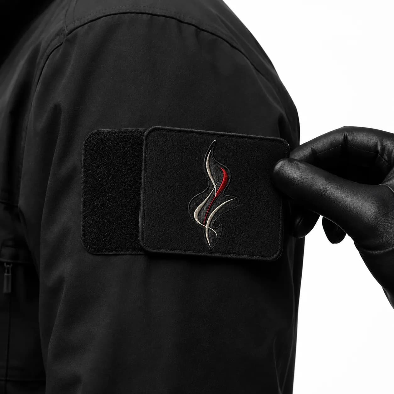 Main gantée décollant un écusson rectangulaire d'une bande velours noire cousue sur la manche d'une veste, la moitié du champ velcro apparaissant sous la pièce